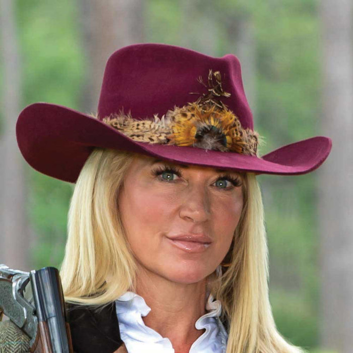 Burgundy cashmere wool Cassidy cowboy hat featuring a decorative feather band on a woman with blonde hair.