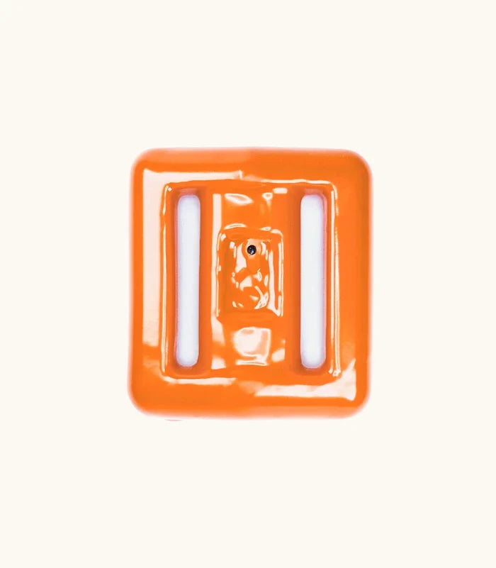Close-up of a glossy orange plastic buckle used with Clownfish Dive Weights by Bright Buoy Diving, shown against a clean off-white background.