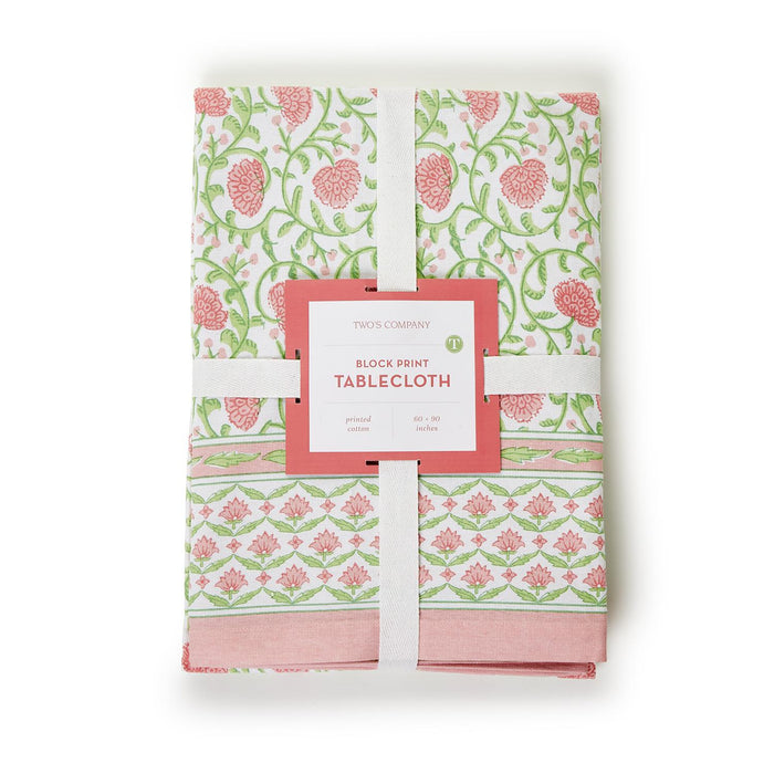 Folded 60x90 cotton tablecloth with a pink and green floral block print pattern and a branded product label.