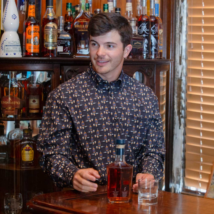 Man wearing a smoke-colored, moisture-wicking long sleeve performance shirt with a bourbon bottle print at a bar.