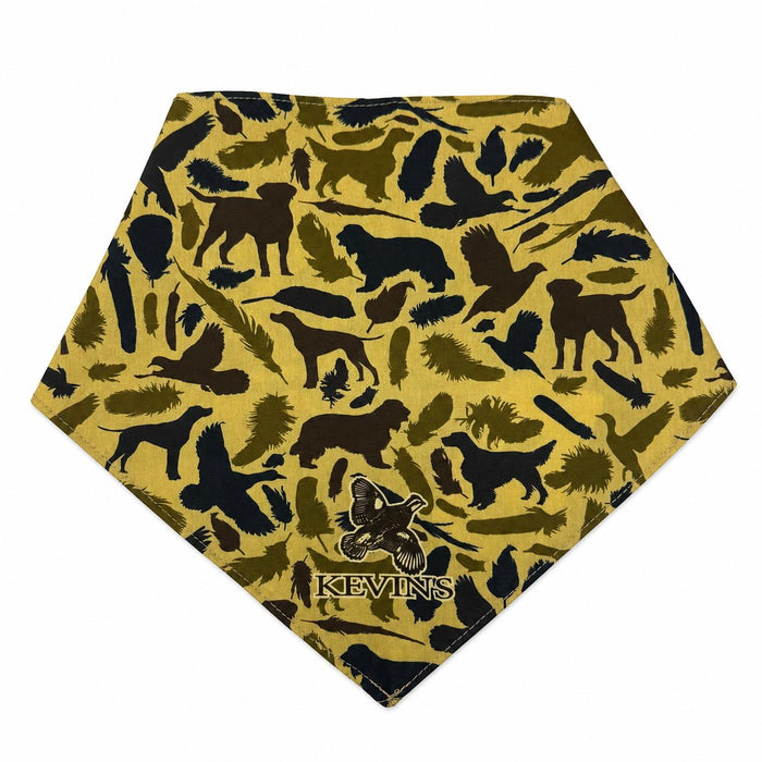 Triangle-shaped dog bandana in mustard yellow with a brown hunting-themed print of dogs, birds, and feathers, featuring Kevin's logo.