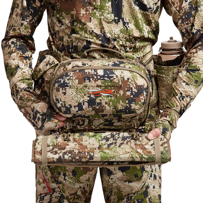 Sitka Turkey Tool Belt in camo print with a front call pocket and removable seat pad worn by a hunter.