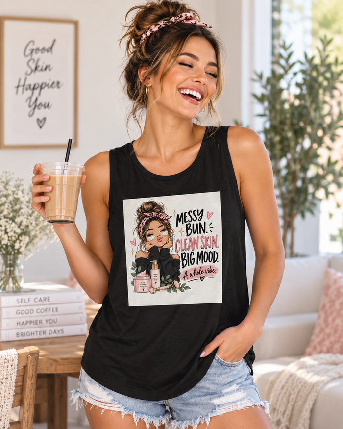 Laughing woman with a messy bun wearing a black Women’s Flowy Muscle Tank featuring the “Messy Bun, Clean Skin, Big Mood” self-care graphic.