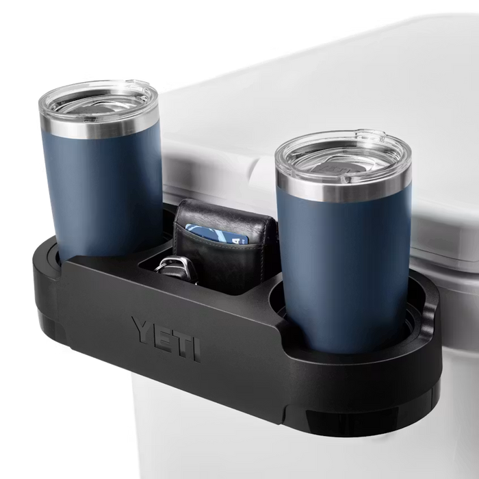 Black YETI Roadie cooler cup caddy attached to a white cooler, holding two blue tumblers and a wallet in the center tray.