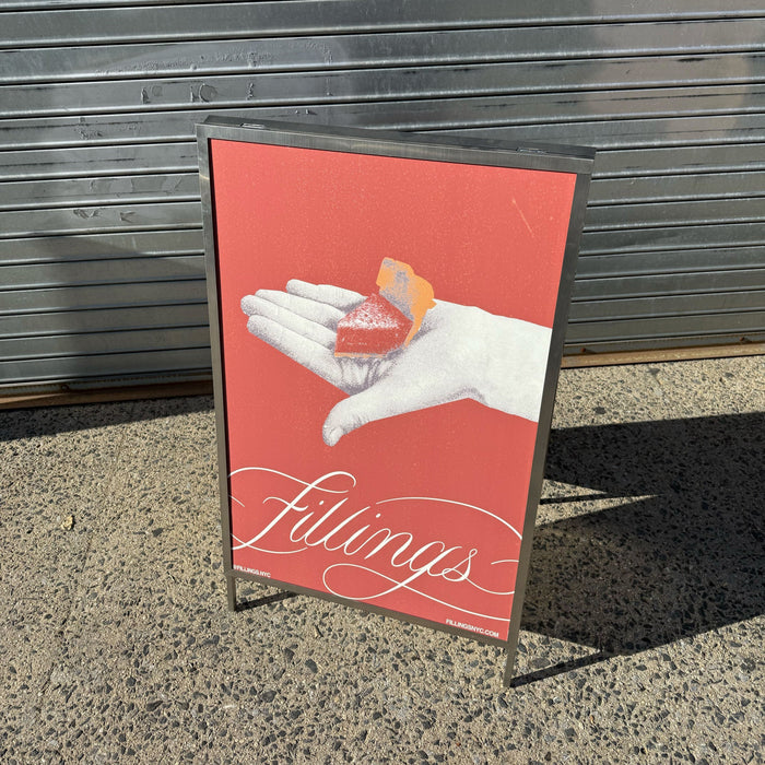 Front angled view of a metal A-frame holder with a red Fillings poster.