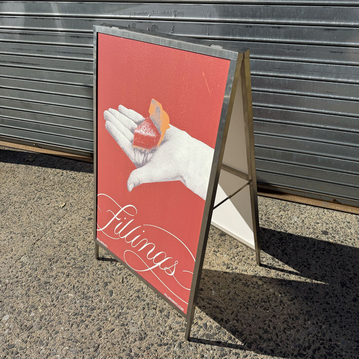 Side view of an A-frame holder with a red Fillings poster, showing the support brace.
