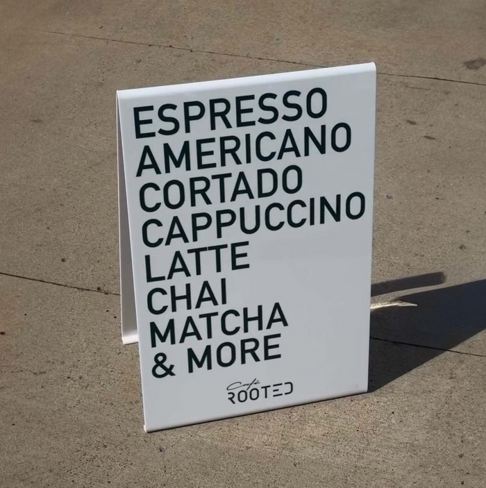 White opaque acrylic A-frame sign listing coffee drinks for Rooted.