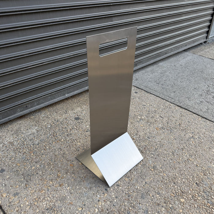 Stainless steel floor sign with a handle cutout displayed outdoors.