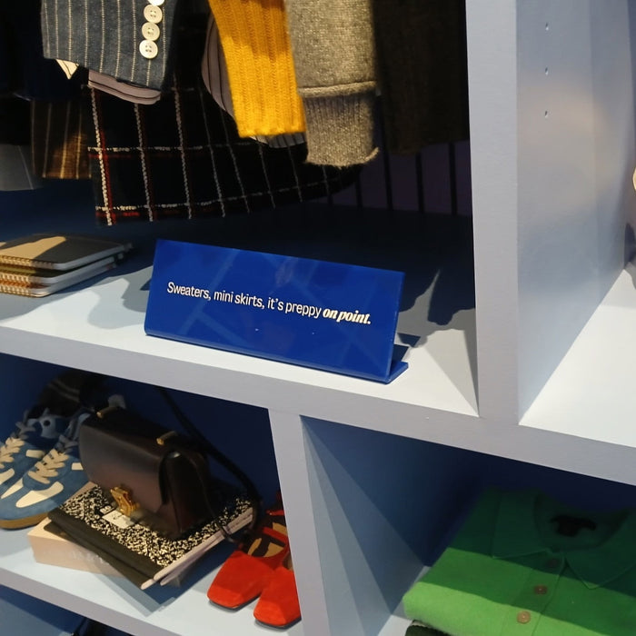 Blue landscape acrylic sign displayed on a clothing-store shelf.
