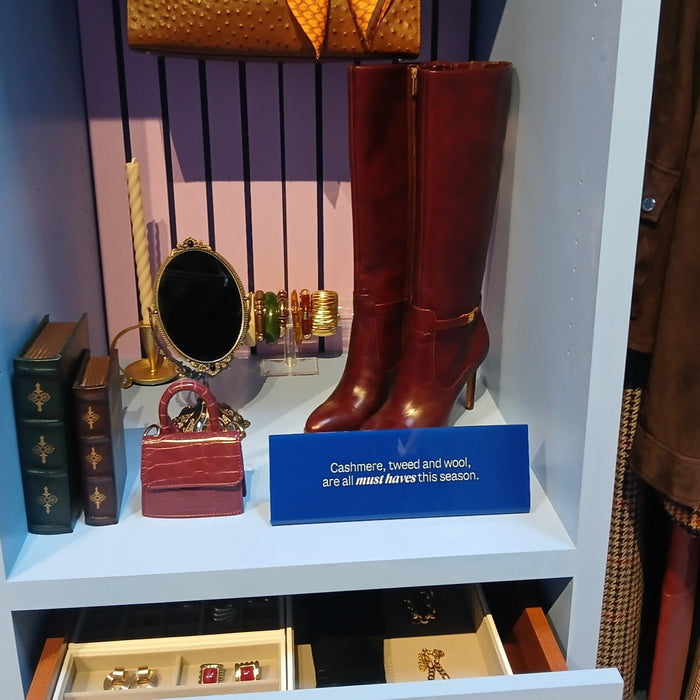 Blue landscape acrylic sign beneath tall red boots in a retail display.