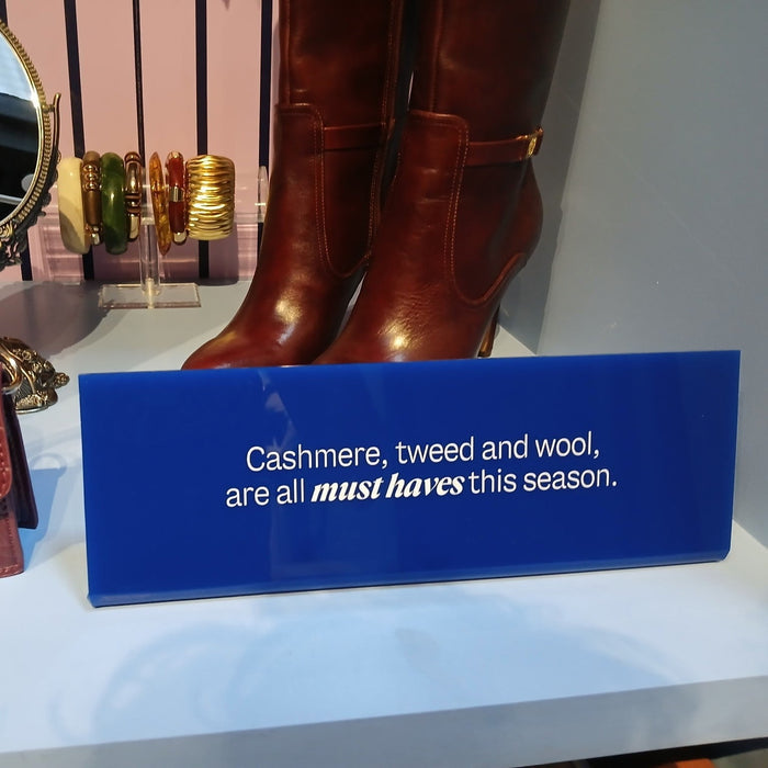 Close-up of a blue acrylic sign describing seasonal cashmere, tweed, and wool.