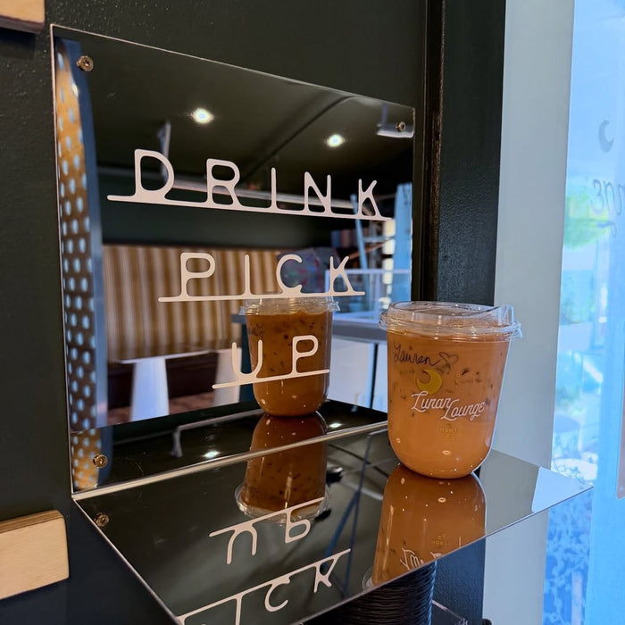 Mirrored wall drink shelf holding a cold drink beneath Drink Pick Up lettering.