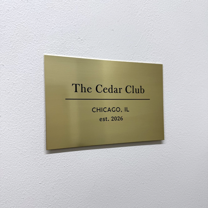 Front angled view of a brass plaque with The Cedar Club lettering.