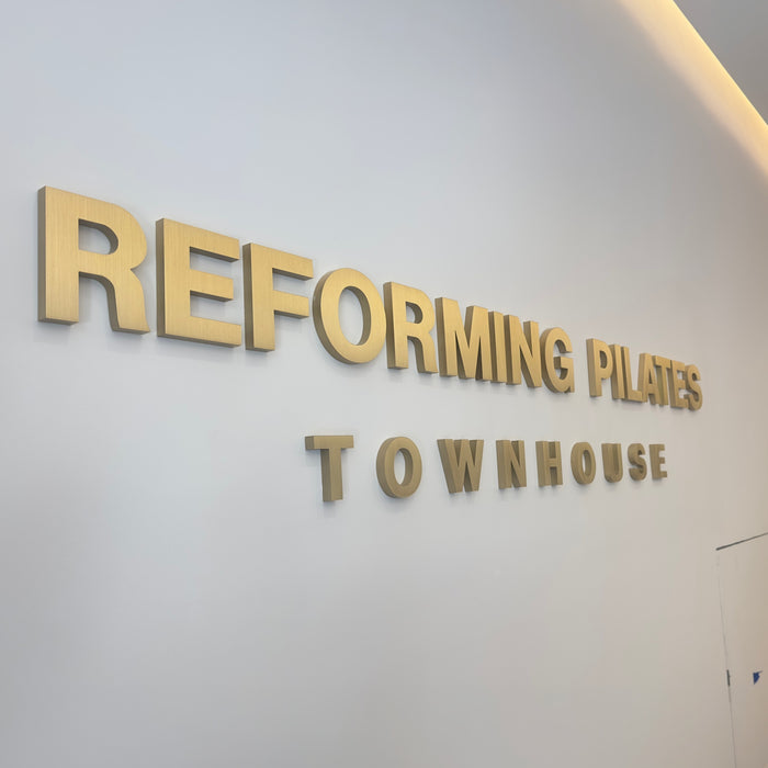 Brass wall letters spelling Reforming Pilates Townhouse, viewed at an angle.