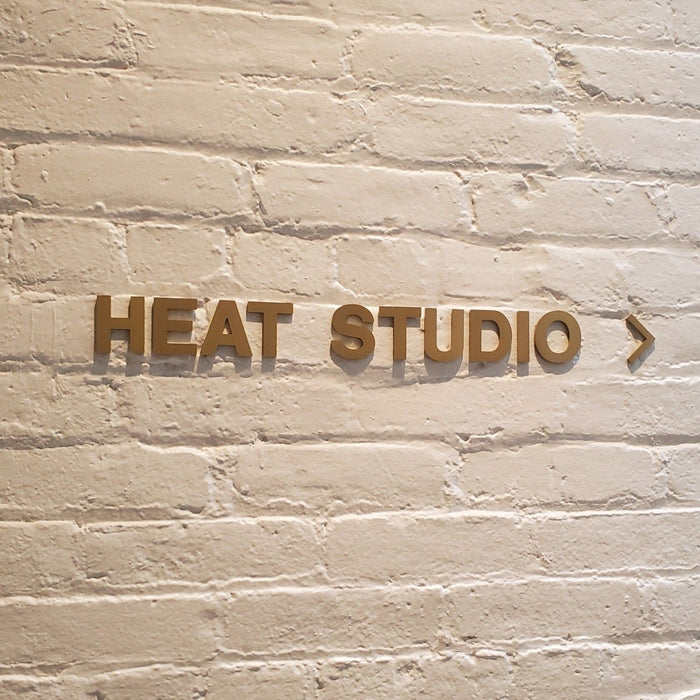 Brass Heat Studio lettering and a right arrow mounted on a brick wall.
