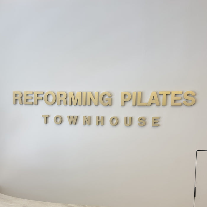 Front view of brass wall letters spelling Reforming Pilates Townhouse.
