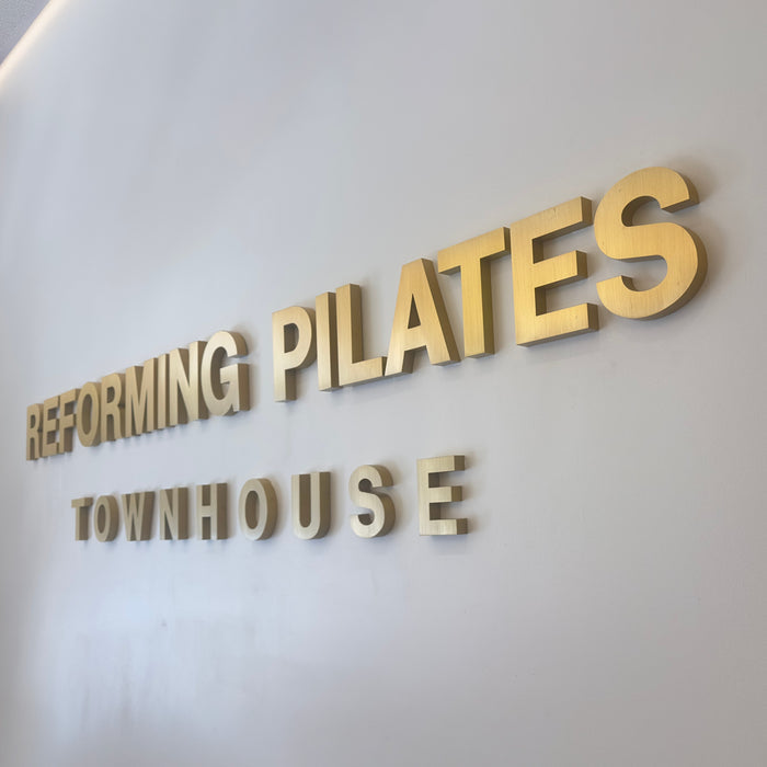 Angled close-up of brass Reforming Pilates Townhouse lettering on a wall.