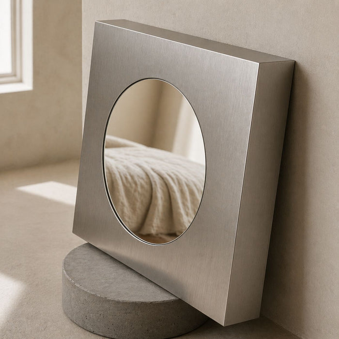 Angled close-up of a square Forma mirror showing its brushed frame and circular inset.