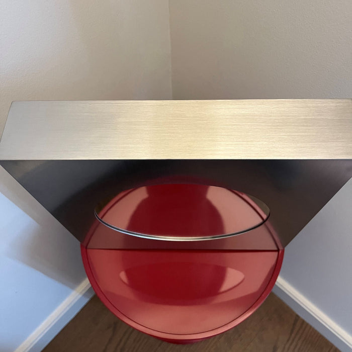 Top view of a square stainless steel Forma mirror on a red table.