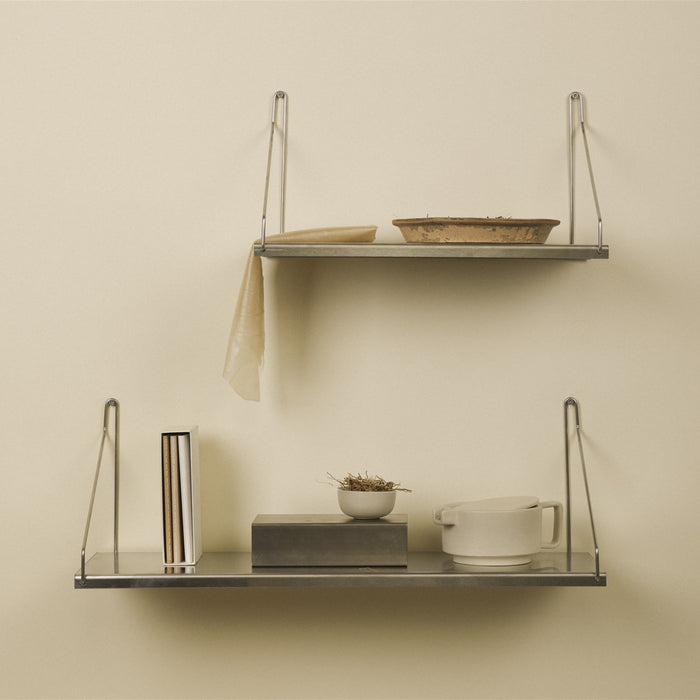 Two stainless steel wall shelves with wire brackets displaying dishes.