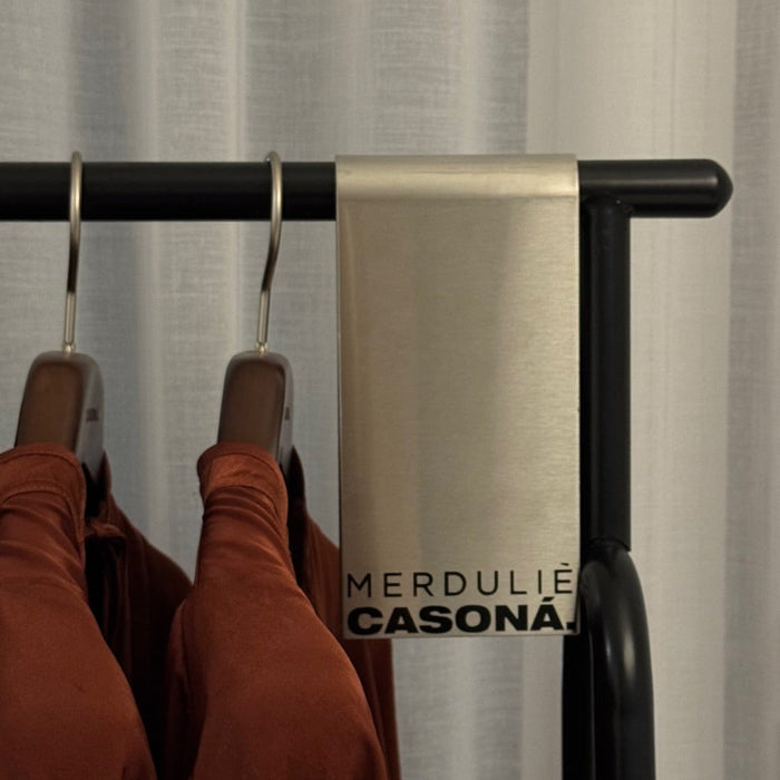 Metal sign clip with Merdulié and Casona lettering beside clothes hangers.