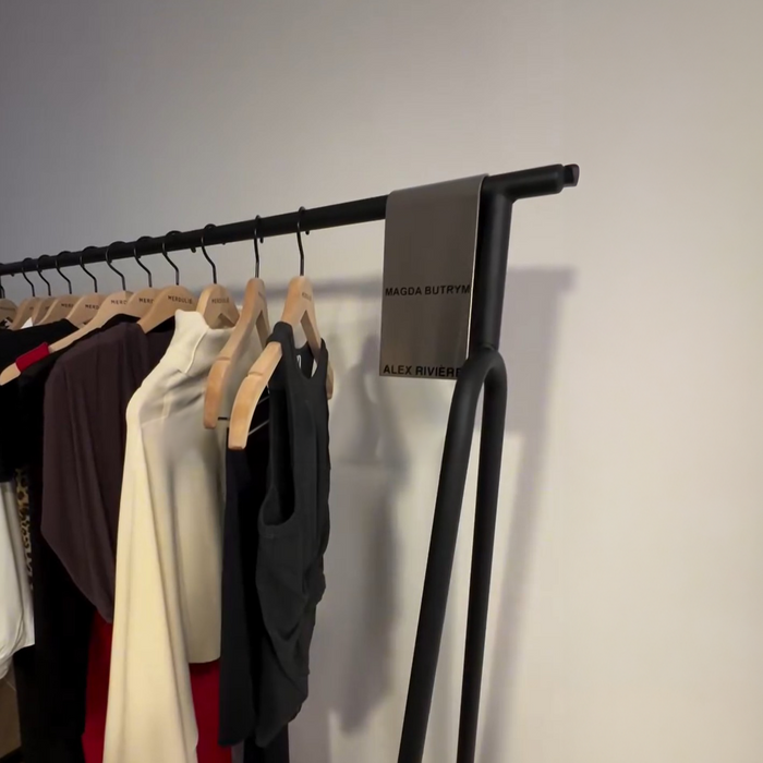 Metal sign clip at the end of a clothing rack displaying neutral-colored garments.