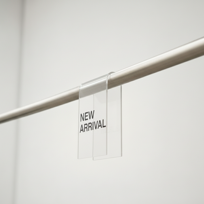 Clear acrylic clothing rack clip with New Arrival lettering on a rail.