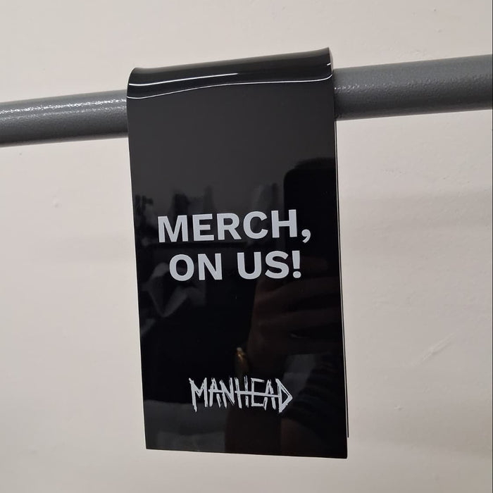 Black acrylic clothing rack clip with Merch, On Us lettering and a Manhead logo.