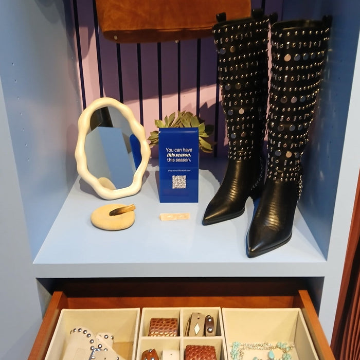 Blue acrylic sign with a QR code beside boots and a mirror in a retail display.