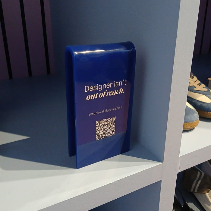 Angled view of a blue acrylic sign with Designer Isn't Out of Reach lettering and a QR code.