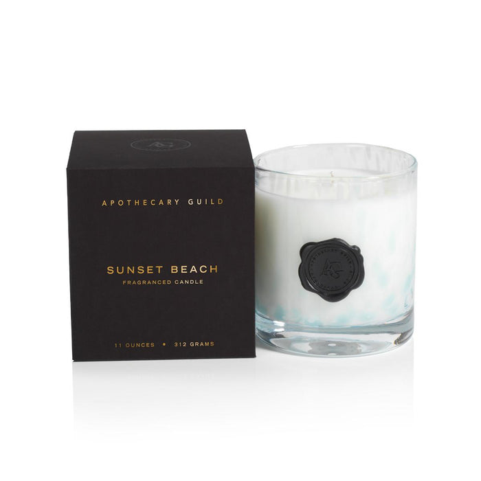 Apothecary Guild Sunset Beach candle in a clear glass jar with a black wax seal next to its premium black presentation box.