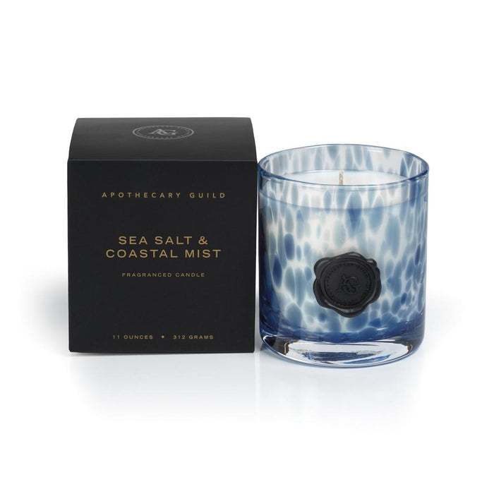Blue and white speckled glass candle with a black wax seal next to its black presentation box.