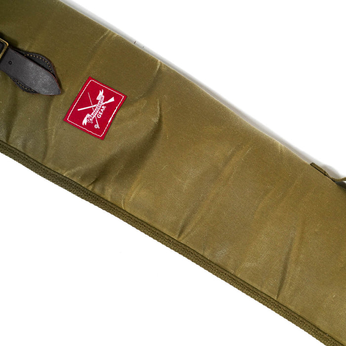 Olive green waxed canvas shotgun case with leather strap, brass hardware, and Armageddon Gear red logo patch.