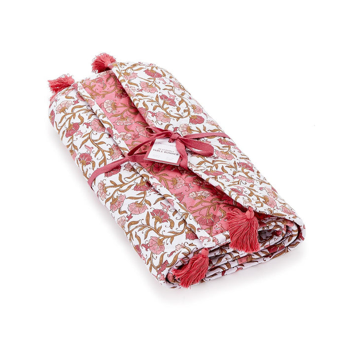 Reversible quilted table runner in blush floral print with pink tassels, 16x72 inches, folded and tied with ribbon.