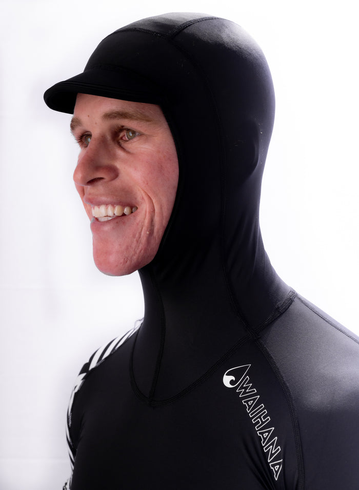 Smiling man wearing a black Waihana Carvico hooded surf rashguard with a structured brim, shown in close-up profile against a white studio background.