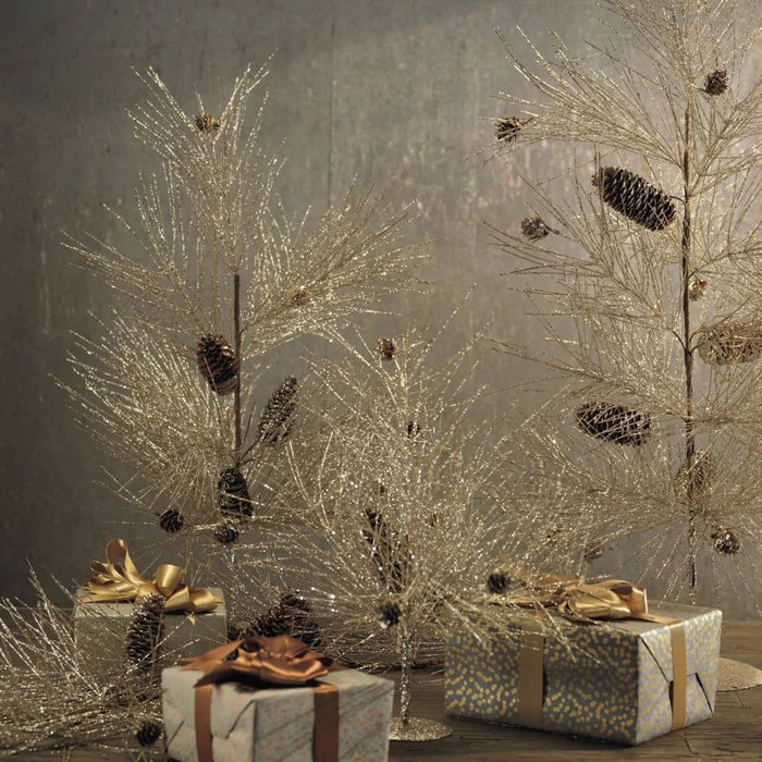 Champagne-colored spruce trees with pinecone accents and metal bases displayed with wrapped holiday gifts.