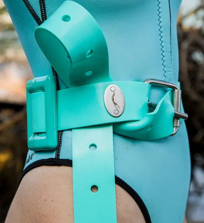 Close-up of a teal rubber Crystal River dive weight belt with a silver Waihana oval buckle medallion, fastened around the hip of a model wearing a matching aqua wetsuit.