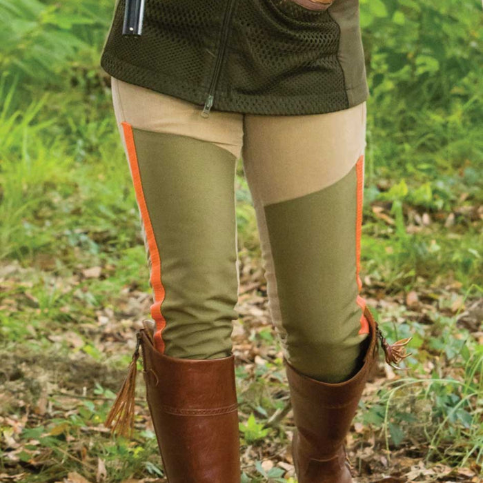 Tan and olive briar pants with bright orange trim accents worn with brown leather boots in a field.