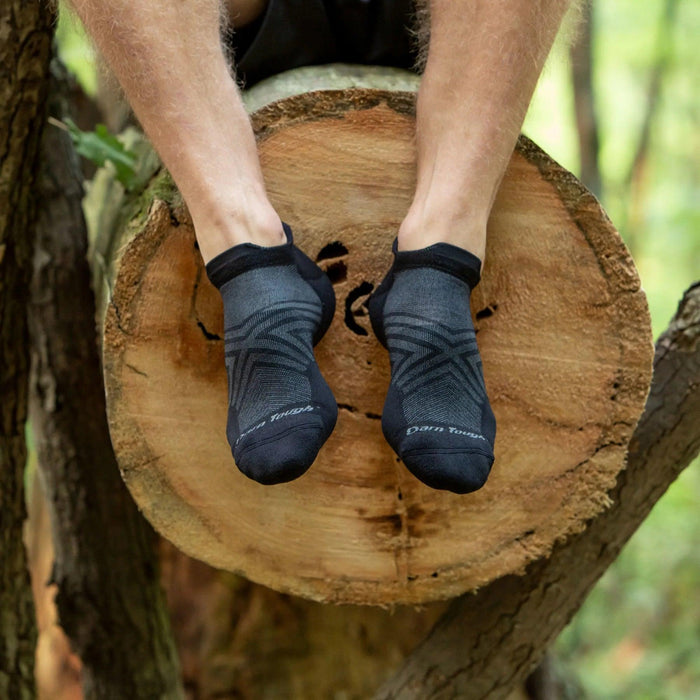 Black Darn Tough ultralight Merino wool running socks with a cushioned heel tab, worn on a runner perched on a tree log.