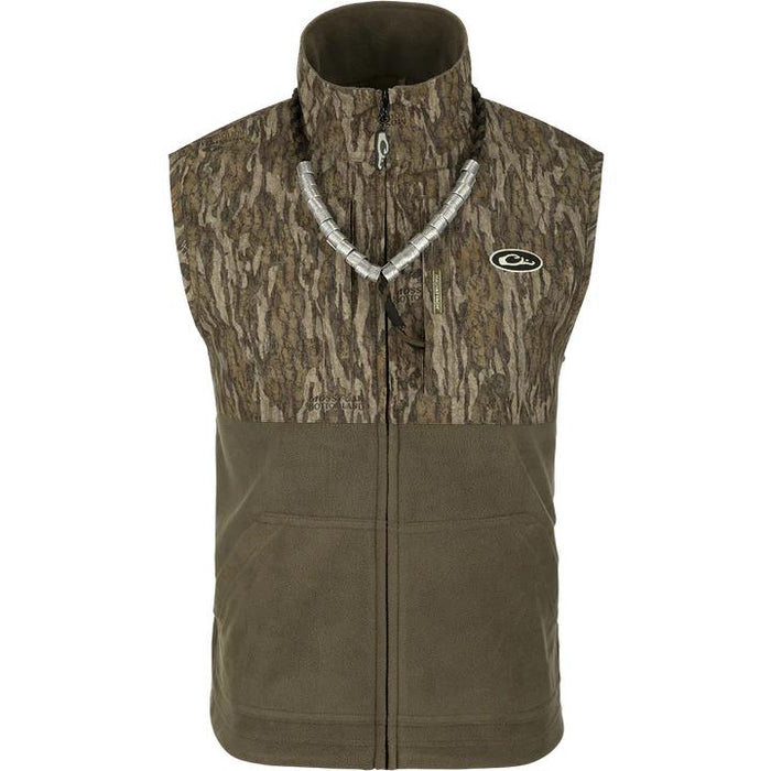 Drake MST Eqwader hunting vest with camo upper, olive fleece lower, zippered chest pockets, and duck call lanyard.