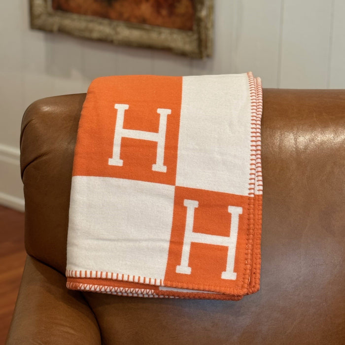 Orange and white equestrian-style blanket with H pattern draped over a brown leather chair.