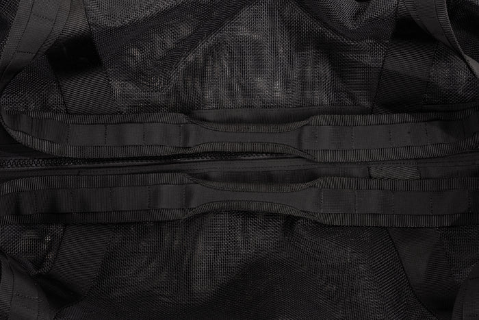 Close-up of a black gear bag showing mesh fabric, woven webbing straps, and a central zipper pocket detail.