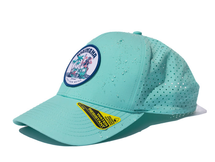 Teal Waihana Hula Diver Hydro Hat with perforated side panels and water droplets beading on the surface, featuring a circular hula diver embroidered patch and a water-resistant hang tag on the brim.