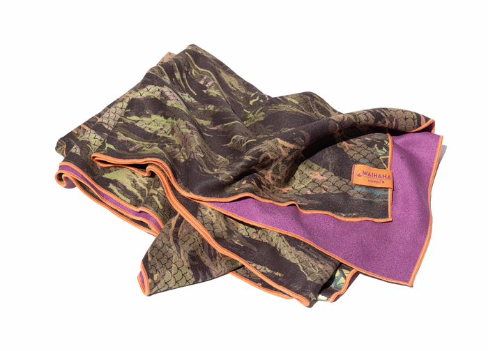 Waihana HydroTech Tropicam Towel folded on a white background, featuring a dark camouflage print on one side and a purple microfiber interior with orange border stitching and an orange Waihana Hawaii woven label.