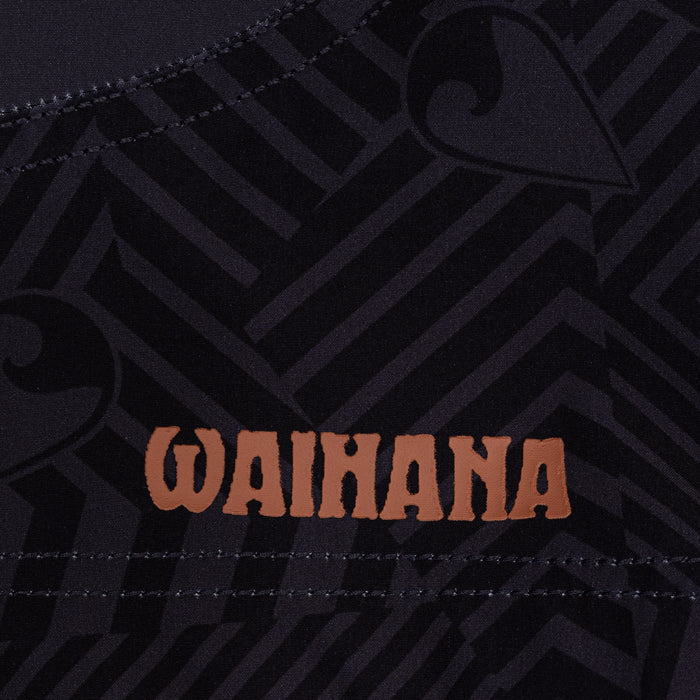 Close-up of the Waihana Jet Black W1-PRO board shorts featuring a dark tonal tribal pattern and a copper-colored Waihana brand logo heat-pressed onto the fabric.