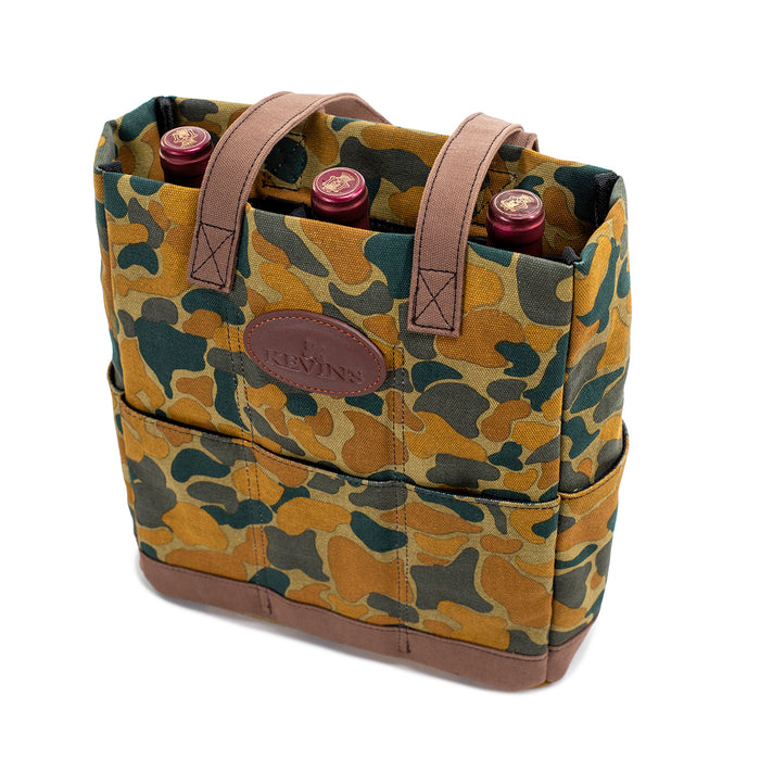 Durable camo canvas wine tote with brown leather trim, exterior pockets, and padded interior holding three wine bottles.