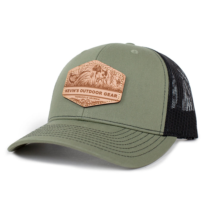 Olive green Richardson 112 trucker cap with a black mesh back and a leather etched pointer dog patch on the front.