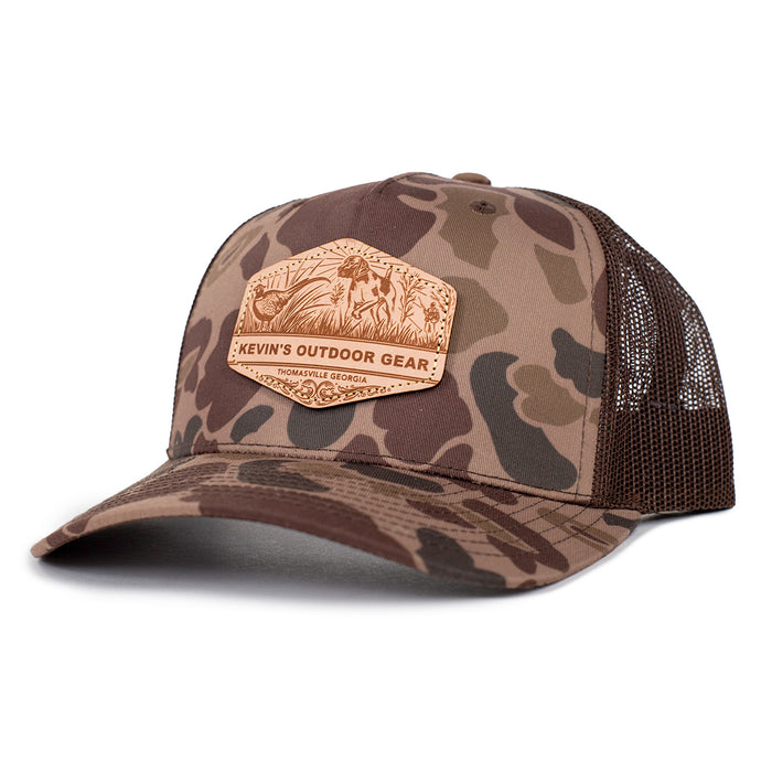 Camo Richardson 112 trucker cap featuring a brown leather patch with a pointer dog and pheasant hunting scene.