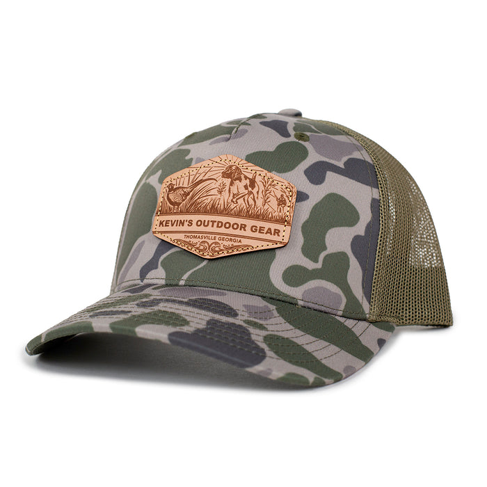 Camo Richardson 112 trucker cap with an etched leather patch featuring a pointer dog and Kevin's Outdoor Gear logo.