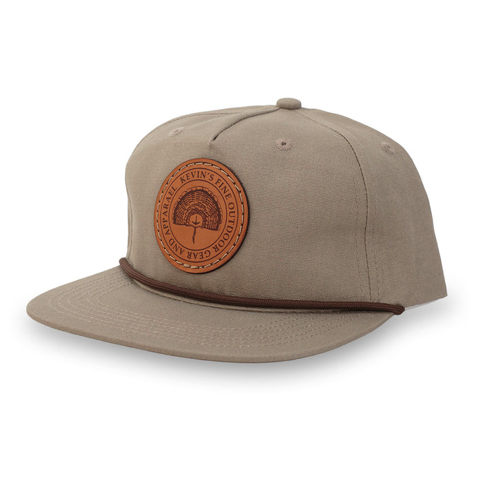 Tan cotton rope cap featuring a round leather patch with a turkey fan design and a brown braided cord on the brim.